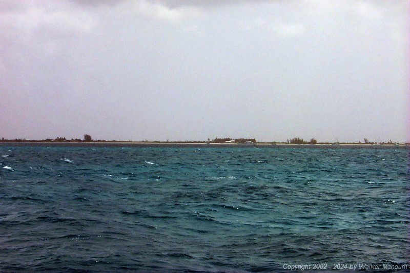 Approaching Anegada. It is slightly hazy and we are 1 mile from the entrance buoys. You can see Setting Point Villa, the Australian pines at Setting Point Villa, the palm trees at Neptune's Treasure, the white roof of Neptune's Treasure, the boat house at Neptune's Treasure, the red entrance buoy, the Australian pines at Whistling Pines, and the Lobster Trap Restaurant.