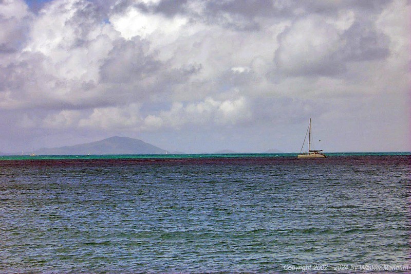 The catamaran continuing its ill-fated approach to Anegada. The skipper of this catamaran was apparently navigationally challenged, as there is a prominent reef just ahead of him that is preventing him from reaching the beach. We first spotted this catamaran sailing north beyond the west end of Anegada, and knew that he had missed the island. He then turned and attempted to approach the island by motoring southeast, directly toward the reef, as shown in this photo. You can see two people up on the bows looking for reef. The reef is visible near the center of this photo, where small waves are breaking.
