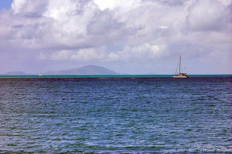 The catamaran continuing its ill-fated approach to Anegada. It is very near the reef now. The skipper of this catamaran was apparently navigationally challenged, as there is a prominent reef just ahead of him that is preventing him from reaching the beach. We first spotted this catamaran sailing north beyond the west end of Anegada, and knew that he had missed the island. He then turned and attempted to approach the island by motoring southeast, directly toward the reef, as shown in this photo. You can see two people up on the bows looking for reef. The reef is visible near the center of this photo, where small waves are breaking. At this point, Walker thought that he was documenting a shipwreck-in-progress.